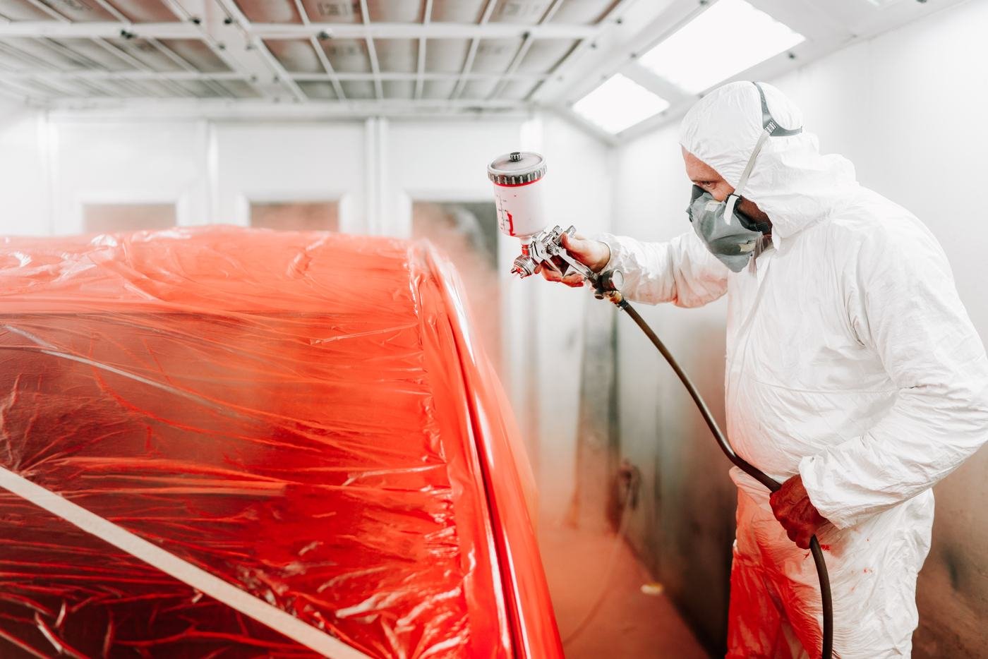 Profissional pintando um carro vermelho dentro da cabine de pintura