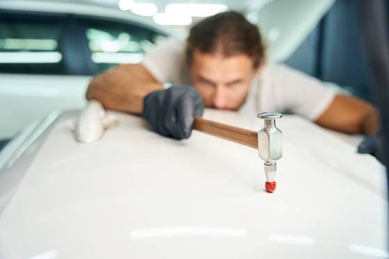 Técnico trabalhando a chapa de um painel por trás, com ferramenta de martelinho