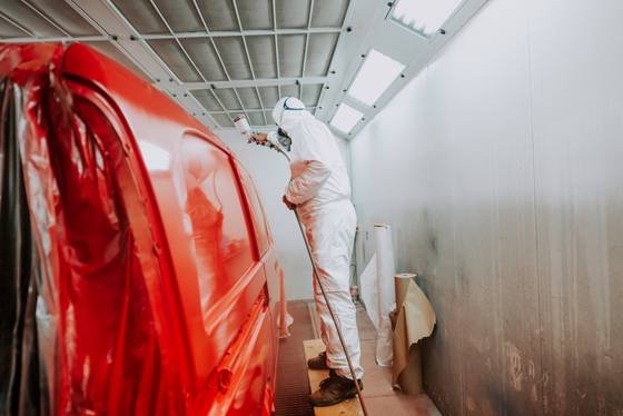 Pintor aplicando tinta em uma peça de carro dentro da oficina